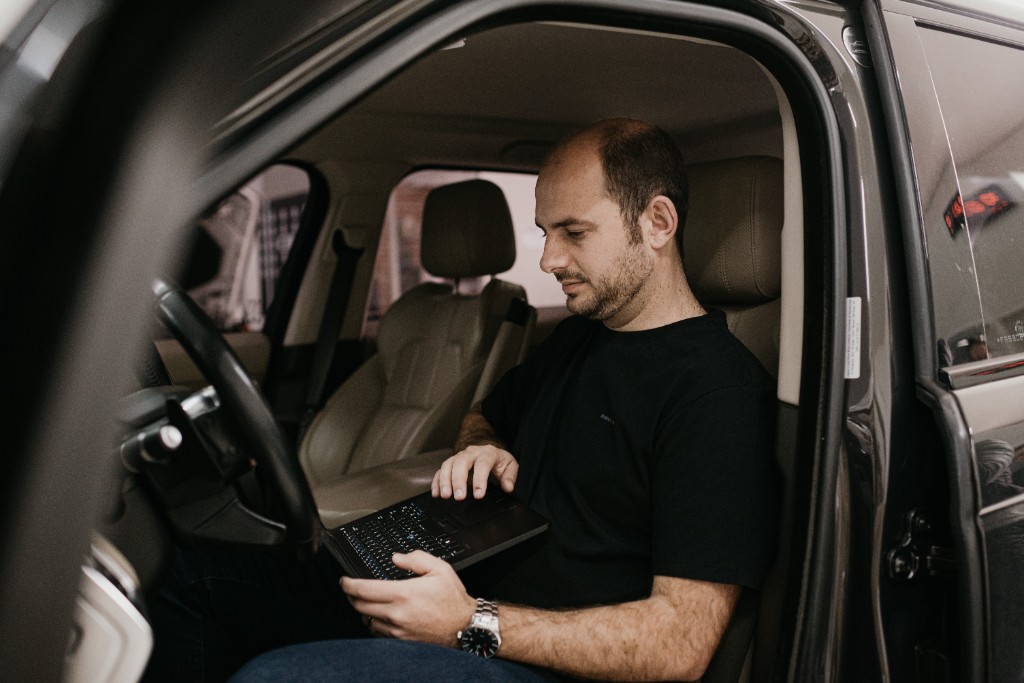 Thiago Dotta no banco do carro, trabalhando no notebook